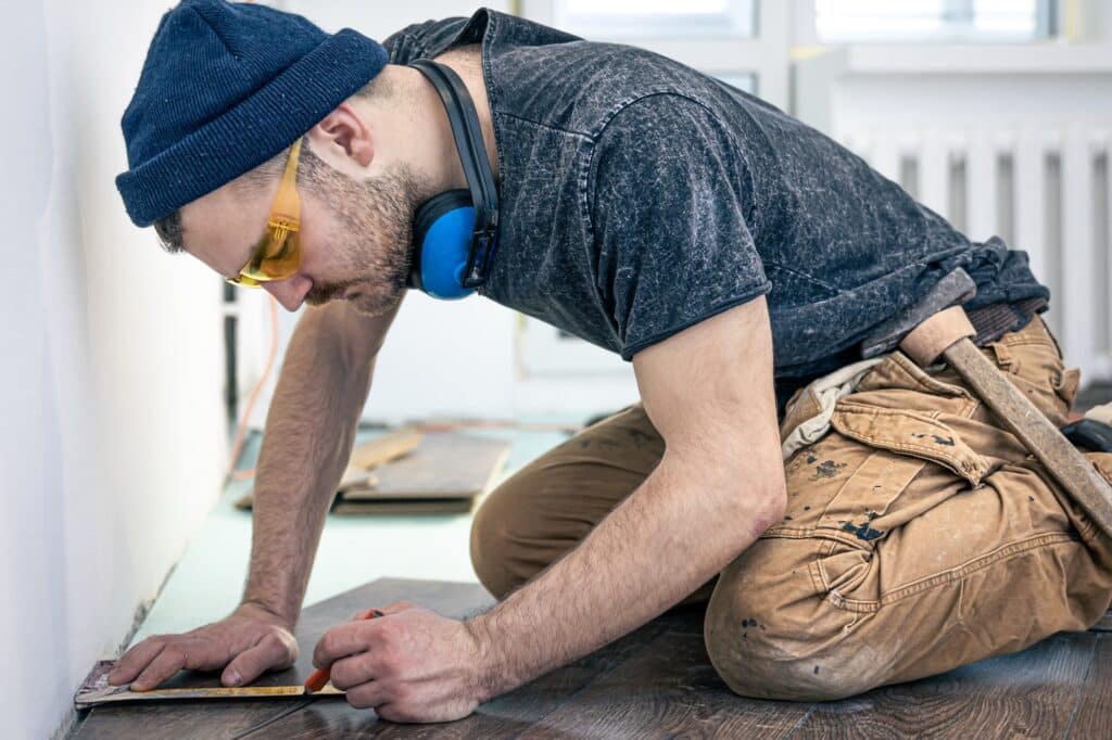 A construction worker installs laminate flooring in a bright room, illustrating durable renovation ideas ideal for student housing rentals in college towns.