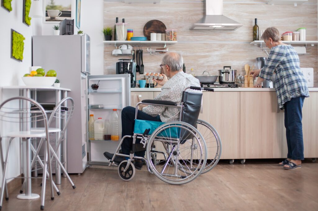Man in a wheelchair helping his wife cook in the kitchen is a visualization of accessible home design needs.
