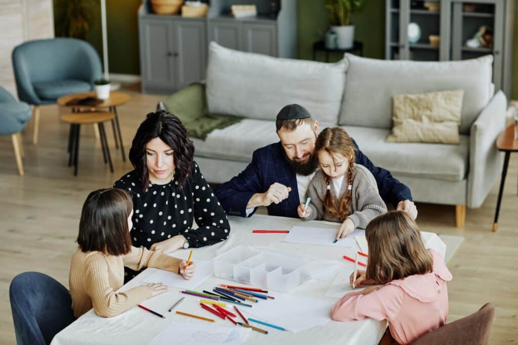 A family of five sits at a table in a cozy living room, engaged in drawing and coloring together, demonstrating family-centered home design with space for creativity and connection.