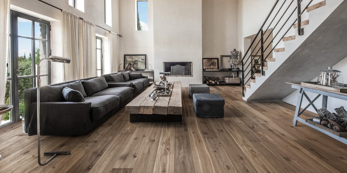 Rustic-modern living room with medium-tone hardwood flooring ideas by Reflex Builders, featuring exposed beams, natural textures, and industrial accents.