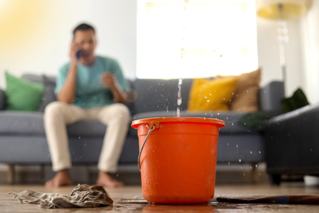 Tenant calling for help as water leaks from the ceiling into an orange bucket—highlighting the need for professional repairs for rental properties.